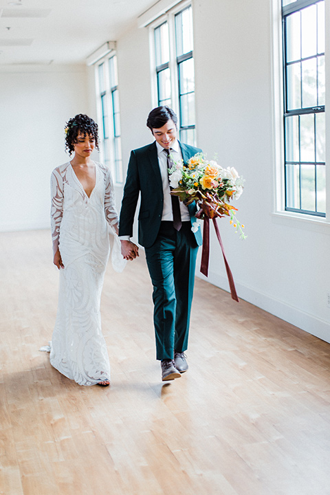 modern Moroccan shoot bride and groom walking by the windows the bride in a white lace gown with long sleeves and a v neck line and the groom is in a green suit with a brown long tie