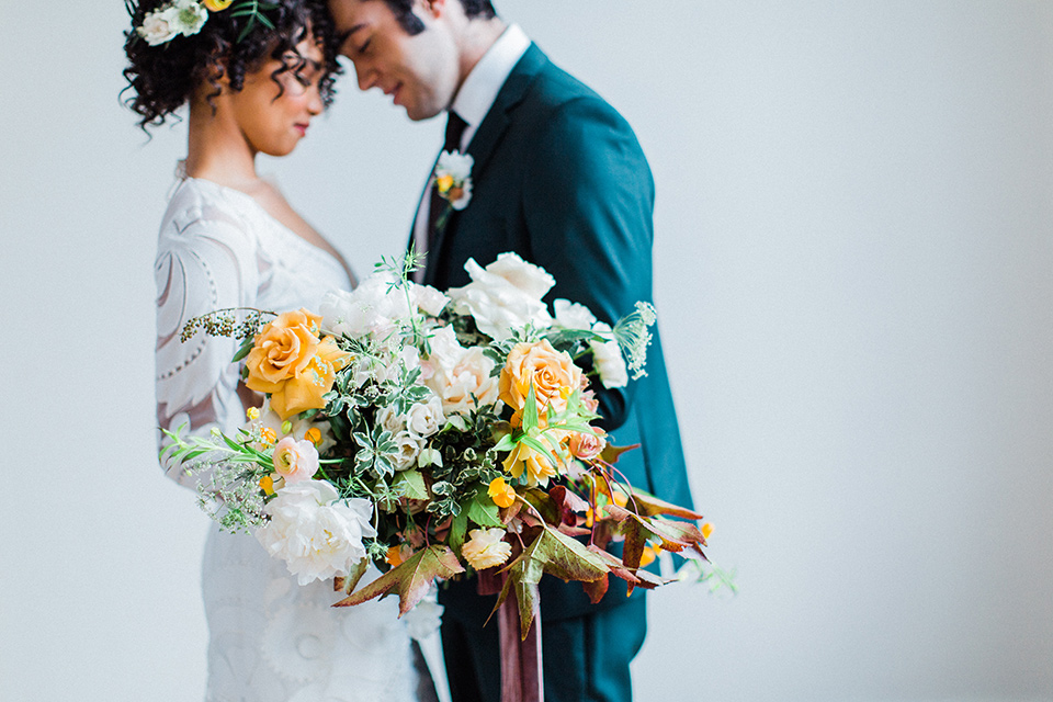 modern Moroccan shoot bride and groom touching heads close up the bride in a white lace gown with long sleeves and a v neck line and the groom is in a green suit with a brown long tie