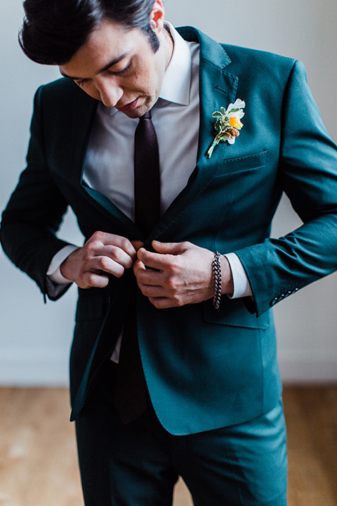 modern Moroccan shoot groom buttoning his jacket in a green suit with a brown long tie