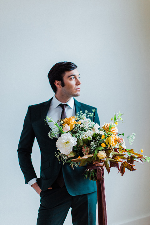 modern Moroccan shoot groom holding flowers in a green suit with a brown long tie