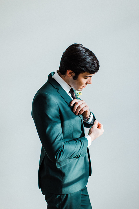 modern Moroccan shoot groom fixing sleeves in a green suit with a brown long tie