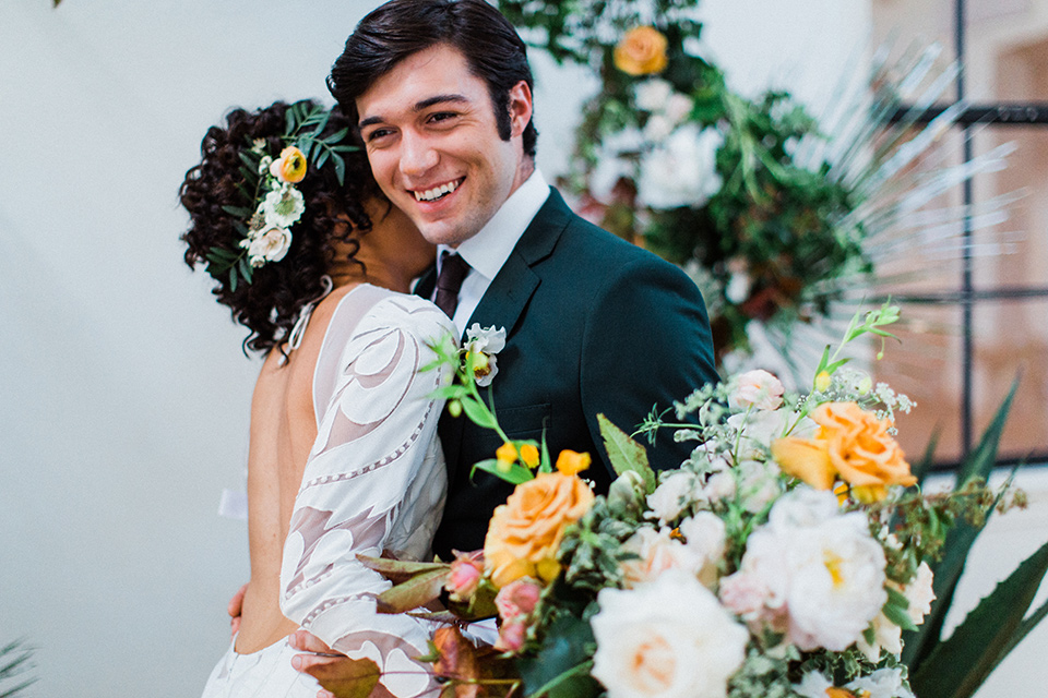 modern Moroccan shoot bride and groom touching smiling the bride in a white lace gown with long sleeves and a v neck line and the groom is in a green suit with a brown long tie