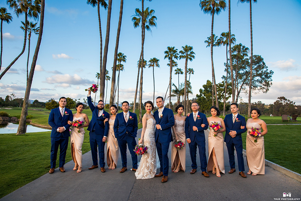 bride in a white lace strapless gown and groom in a blue suits and groomsmen in blue suits and bridesmaids in champagne gowns 