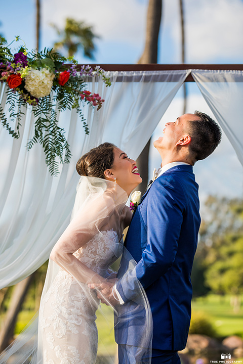  bride in a white gown with a lace strapless neckline and the groom in a blue suit 