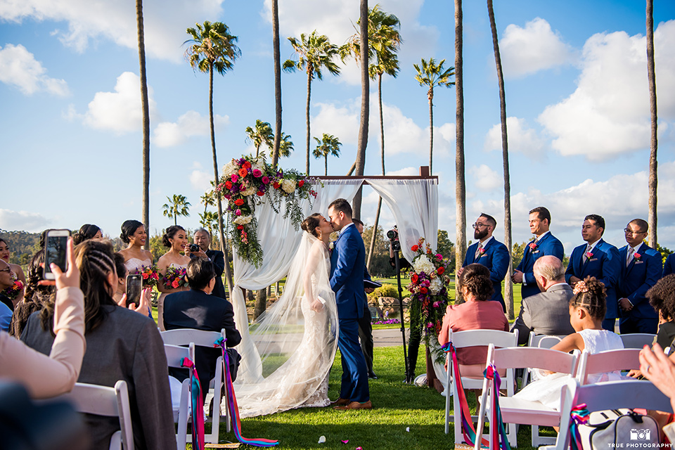 bride in a white lace strapless gown and groom in a blue suits and groomsmen in blue suits and bridesmaids in champagne gowns 