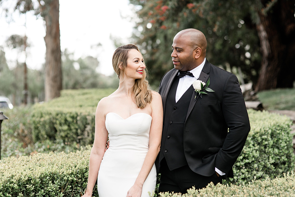 Oak-Meadows-Shoot-bride-and-groom-walking-by-hedges-bride-in-a-white-strapless-lace-gown-groom-in-a-black-tuxedo-with-a-black-bow-tie