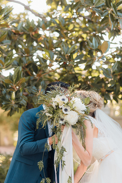 orange-county-wedding-bride-and-groom-behind-flowers-bride-in-a-two-piece-lace-ballgown-groom-in-a-brighter-blue-suit-with-a-flowal-bowtie