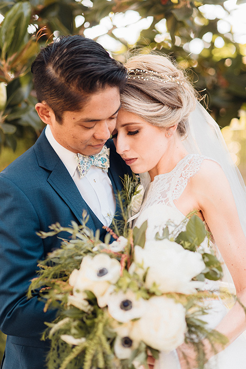 orange-county-wedding-bride-and-groom-touching-heads-bride-in-a-two-piece-lace-ballgown-groom-in-a-brighter-blue-suit-with-a-flowal-bowtie