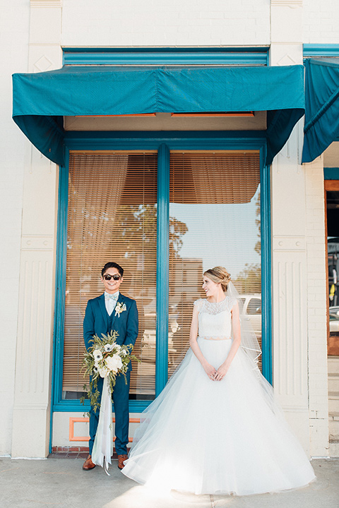 orange-county-wedding-bride-and-groom-under-blue-window-awning-bride-in-a-two-piece-lace-ballgown-groom-in-a-brighter-blue-suit-with-a-flowal-bowtie