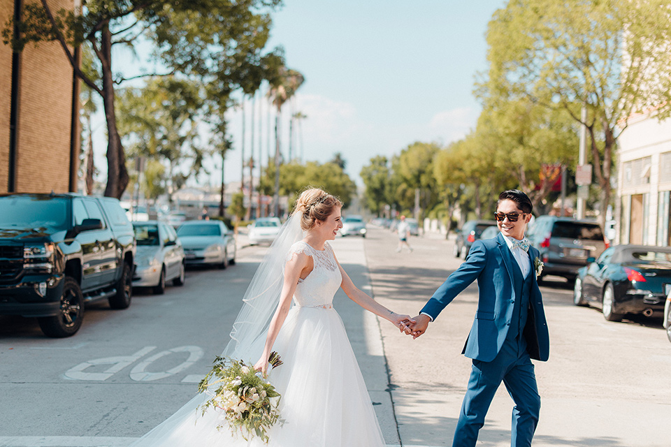 orange-county-wedding-bride-and-groom-walking-across-the-street-bride-in-a-two-piece-lace-ballgown-groom-in-a-brighter-blue-suit-with-a-flowal-bowtie