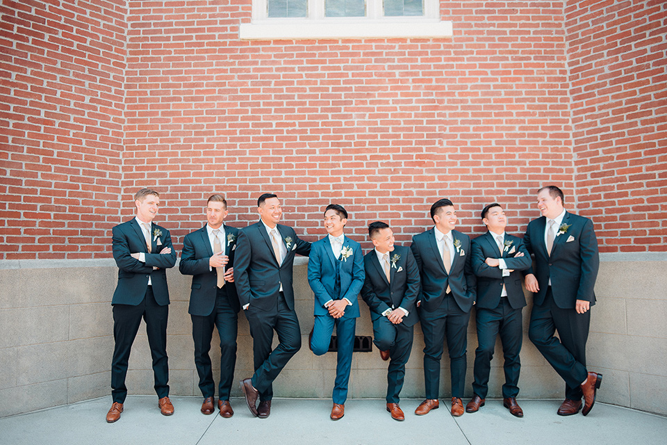 orange-county-wedding-groomsmen-by-brick-wall-groomsmen-in-a-dark-navy-suit-groom-in-a-brighter-blue-suit-with-a-flowal-bowtie