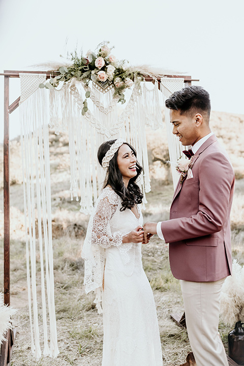 Owl-Creek-Farms-shoot-bride-and-groom-laughing-at-ceremony-bide-in-a-flowing-boho-gown-with-sleeves-groom-in-a-rose-pink-suit-and-velvet-bowtie