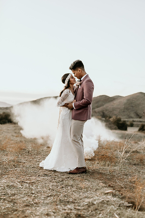 Owl-Creek-Farms-shoot-bride-and-groom-at-ceremony-bride-wearing-a-bohemian-style-dress-with-flutter-sleeves-and-a-macrame-style-headpiece-groom-in-a-rose-pink-suit-jacket-with-tan-pants-and-a-velvet-bow-tie