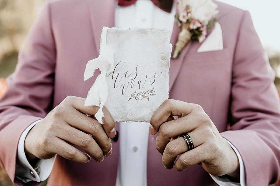 Owl-Creek-Farms-shoot-groom-holding-vow-book-groom-in-a-rose-pink-suit-jacket-with-tan-pants-and-a-velvet-bow-tie