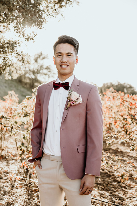 Owl-Creek-Farms-shoot-groom-looking-at-camera-in-a-rose-pink-suit-jacket-with-tan-pants-and-a-velvet-bow-tie
