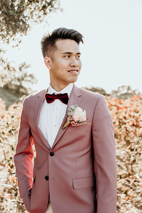 Owl-Creek-Farms-shoot-groom-looking-to-the-side-in-a-rose-pink-suit-and-velvet-bowtie