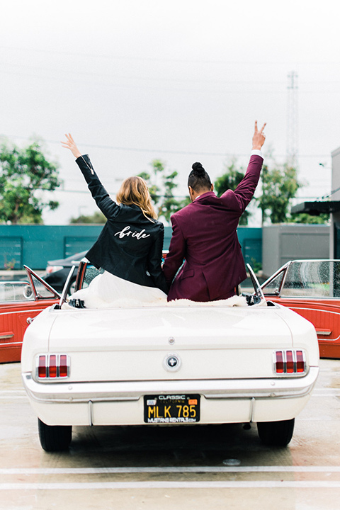 rock-n-roll-wedding-style-bride-and-groom-in-car-bride-in-a-white-flowing-gown-and-a-black-leather-jacket-groom-in-a-deep-burgundy-suit-with-floral-bow-tie