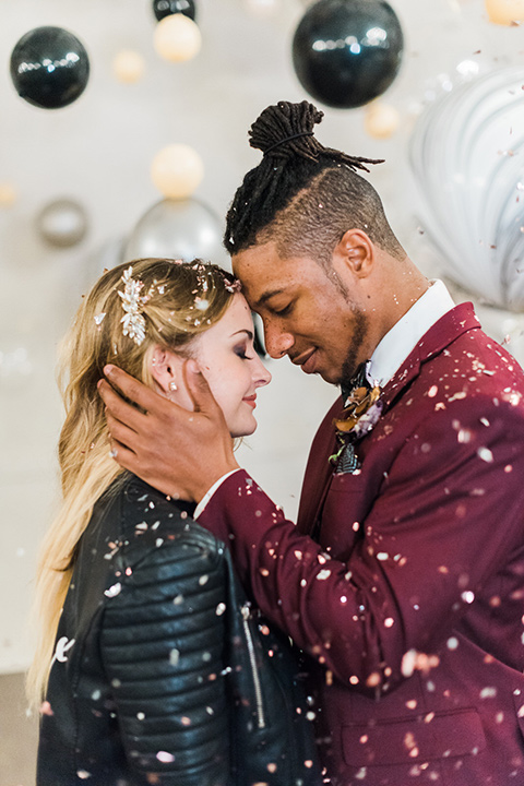 rock-n-roll-wedding-style-bride-and-groom-touching-heads-with-confetti-bride-in-a-white-flowing-gown-and-a-black-leather-jacket-groom-in-a-deep-burgundy-suit-with-floral-bow-tie