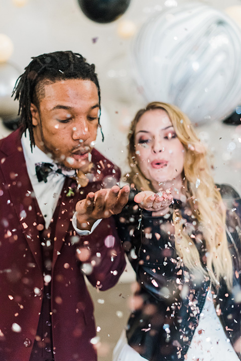 rock-n-roll-wedding-style-bride-and-groom-with-confetti-bride-in-a-white-flowing-gown-and-a-black-leather-jacket-groom-in-a-deep-burgundy-suit-with-floral-bow-tie