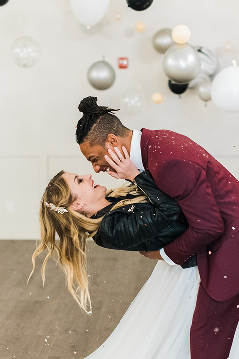 rock-n-roll-wedding-style-groom-dipping-bride-bride-in-a-white-flowing-gown-and-a-black-leather-jacket-groom-in-a-deep-burgundy-suit-with-floral-bow-tie