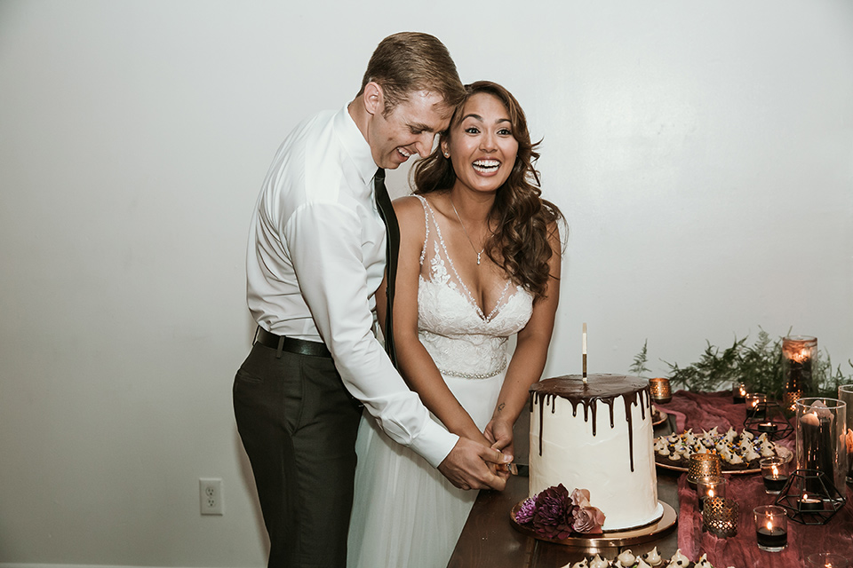 Moniker-Warehouse-Wedding-bride-and-groom-cutting-cake-the-bride-is-in-a-flowing-gown-with-straps-and-a-deep-v-neckline-while-the-groom-wore-a-charcoal-grey-tuxedo-with-a-black-long-tie