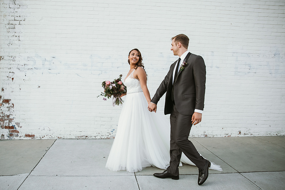 Moniker-Warehouse-Wedding-bride-and-groom-walking-the-bride-is-in-a-flowing-gown-with-straps-and-a-deep-v-neckline-while-the-groom-wore-a-charcoal-grey-tuxedo-with-a-black-long-tie