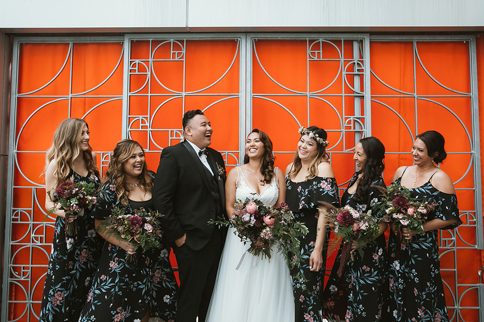 Moniker-Warehouse-Wedding-bridesmaids-and-brideman-bridesmaids-in-black-with-pink-floral-long-gowns-with-a-bridesman-in-a-black-tuxedo-and-the-bride-is-in-a-flowing-gown-with-straps-and-a-deep-v-neckline