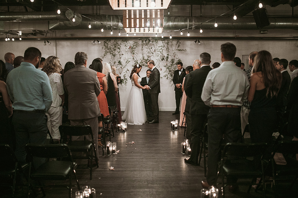 Moniker-Warehouse-Wedding-ceremony-the-bride-is-in-a-flowing-gown-with-straps-and-a-deep-v-neckline-while-the-groom-wore-a-charcoal-grey-tuxedo-with-a-black-long-tie