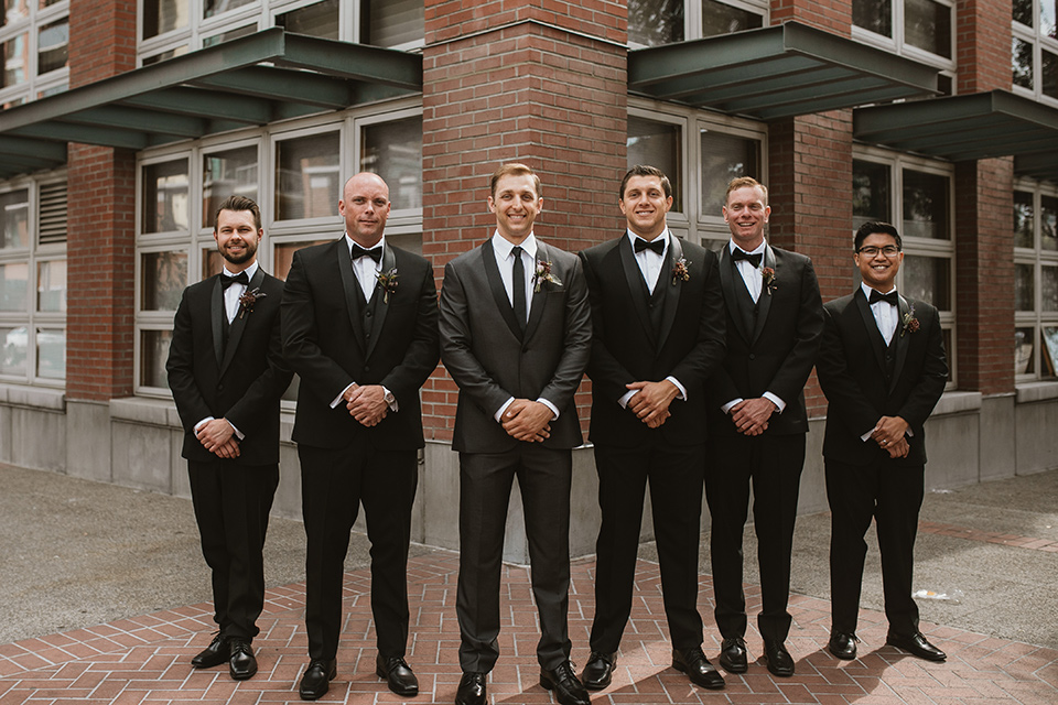 Moniker-Warehouse-Wedding-groomsmen-standing-in-a-line-the-groom-wore-a-charcoal-grey-tuxedo-with-a-black-long-tie-groomsmen-in-black-tuxedos