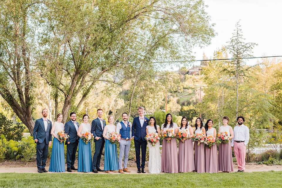 bridesmaids in pink and cream gowns and bridesman in pink pants and white shirt, groomsmen in blue suits and groomsladies in blue skirts and cream tops