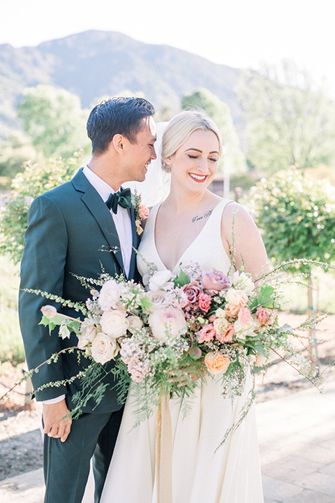  bride in a white ballgown with straps and a deep v neckline and the groom in a dark green suit with a black bow tie 