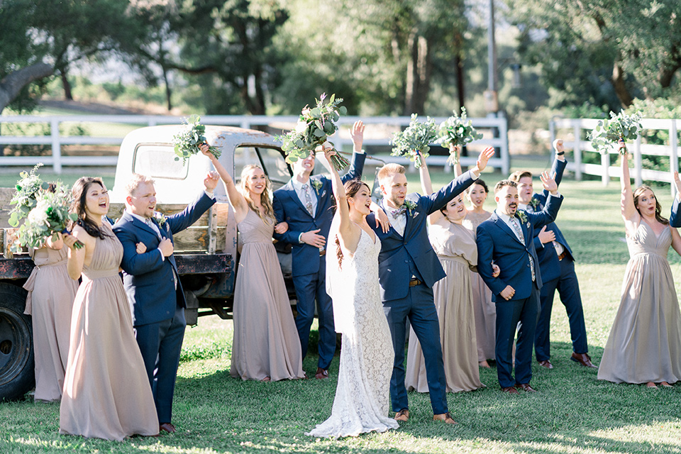 Circle-Oak-ranch-wedding-bridal-party-arms-raised-bridesmaids-in-taupe-colored-long-dresses-groomsmen-in-cobalt-blue-suits-with-floral-long-ties-bride-in-lace-form-fitting-gown-with-thin-straps-and-groom-was-in-a-cobalt-suit-with-a-floral-bowtie