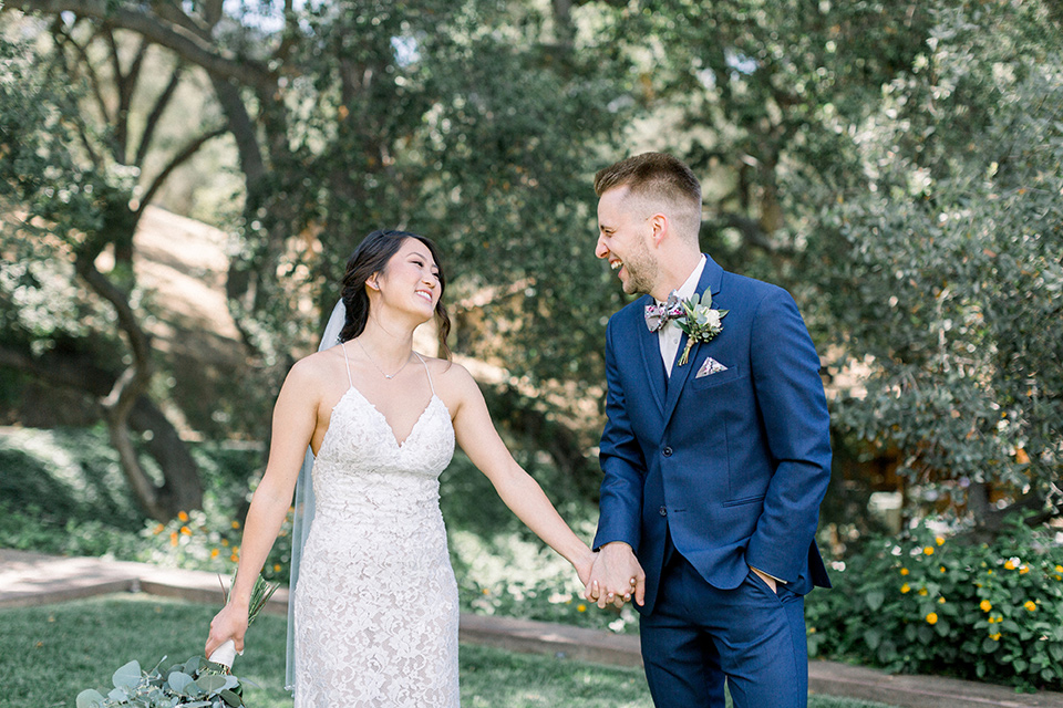 Circle-Oak-ranch-wedding-bride-and-groom-laughing-walking-bride-in-lace-form-fitting-gown-with-thin-straps-and-groom-was-in-a-cobalt-suit-with-a-floral-bowtie