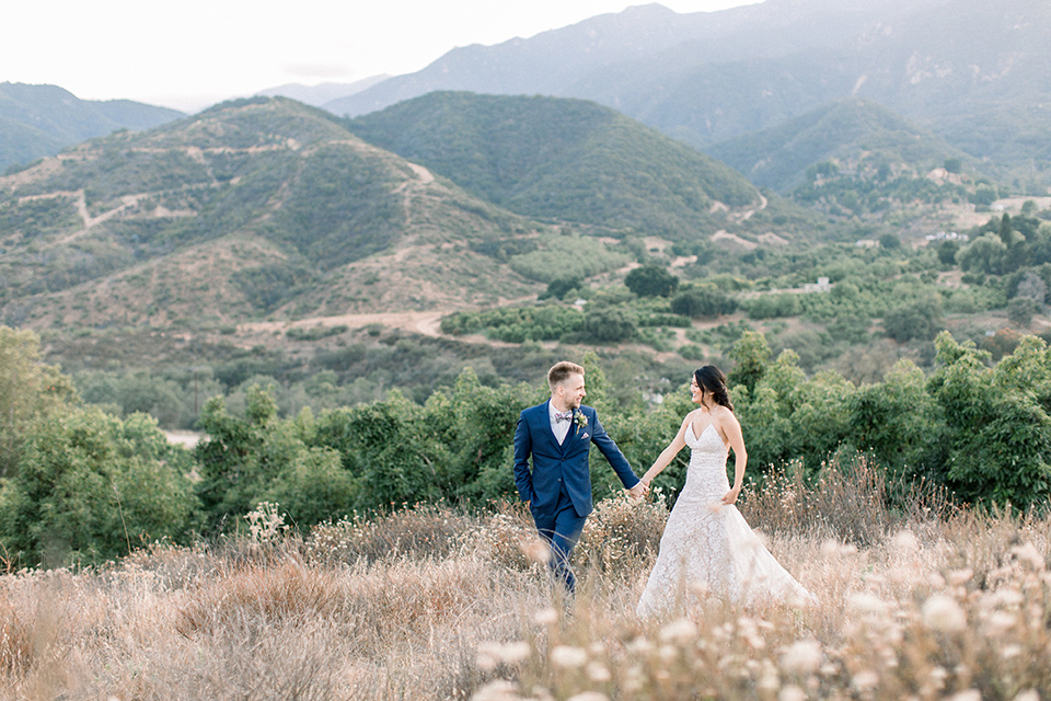 Circle-Oak-ranch-wedding-bride-and-groom-walking-bride-in-lace-form-fitting-gown-with-thin-straps-and-groom-was-in-a-cobalt-suit-with-a-floral-bowtie