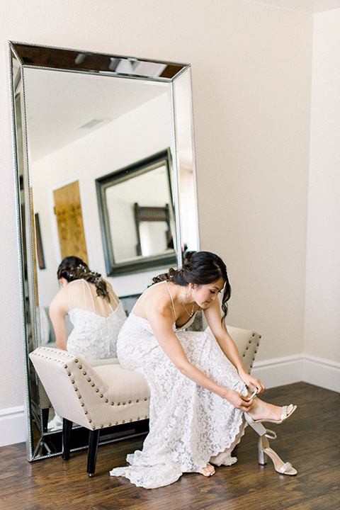 Circle-Oak-ranch-wedding-bride-putting-on-shoes-bride-in-lace-form-fitting-gown-with-thin-straps