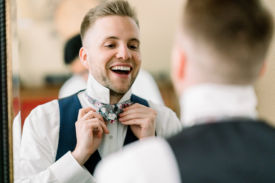 Circle-Oak-ranch-wedding-groom-tying-bow-tie-in-a-cobalt-suit-with-a-floral-bowtie