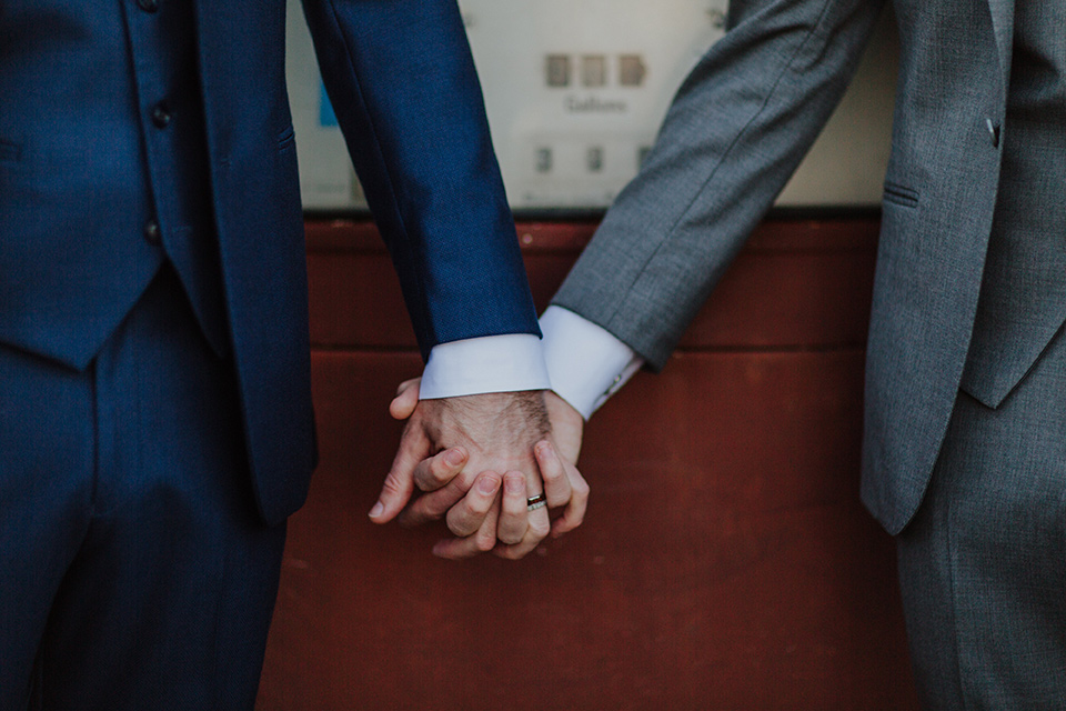 Sunset-Cliffs-Shoot-close-up-on-hands-one-groom-in-a-grey-suit-with-the-other-groom-in-a-blue-suit