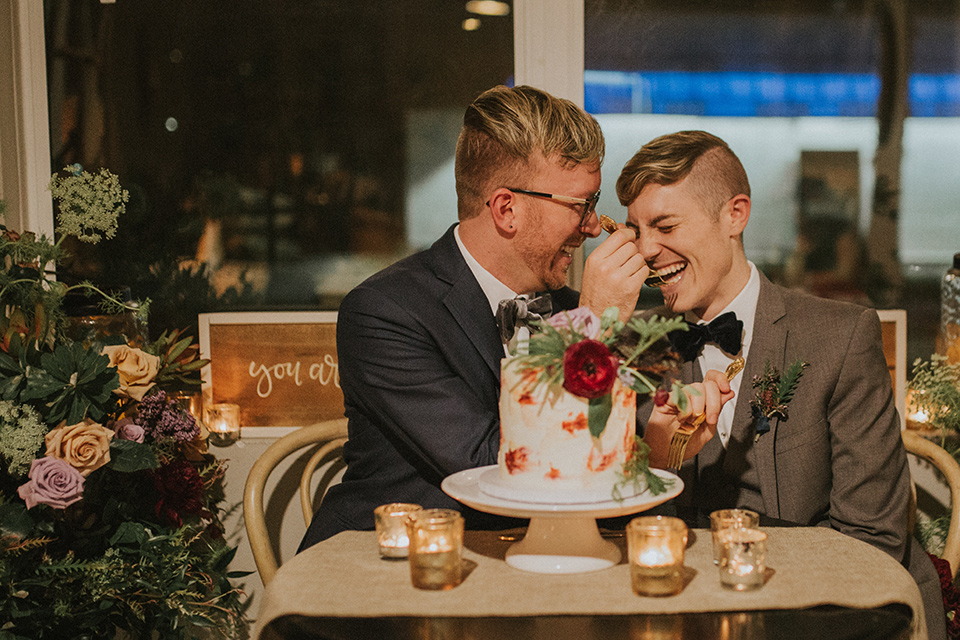 Sunset-Cliffs-Shoot-grooms-at-table-one-groom-in-a-grey-suit-with-the-other-groom-in-a-blue-suit