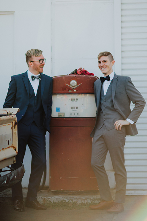 Sunset-Cliffs-Shoot-grooms-by-gas-pump-one-groom-in-a-grey-suit-and-the-other-groom-in-a-blue-suit