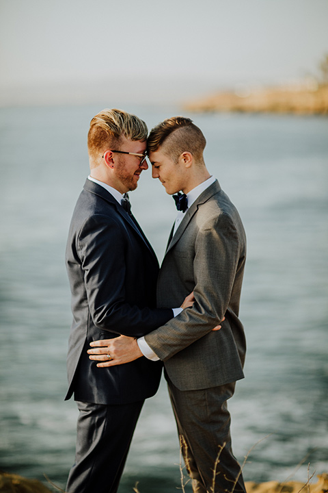 Sunset-Cliffs-Shoot-grooms-touching-heads-one-groom-in-a-grey-suit-and-the-other-groom-in-a-blue-suit
