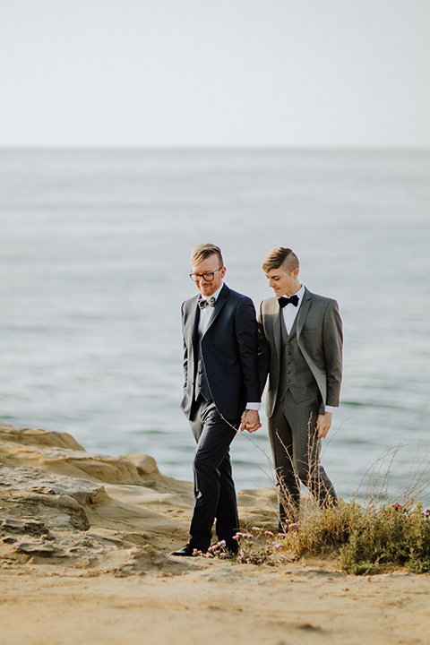 Sunset-Cliffs-Shoot-grooms-walking-by-cliff-one-groom-in-a-grey-suit-and-one-groom-in-a-navy-suit