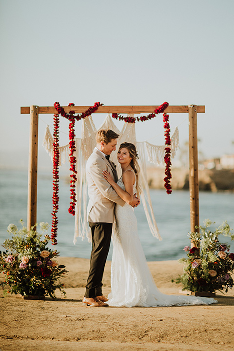 Sunset-Cliffs-Elopement-bride-and0-groom-kiss-at-ceremony-bride-in-a-lace-white-gown-with-thin-straps-groom-in-a-tan-suit-coat-with-black-pants-and-black-bow-tie