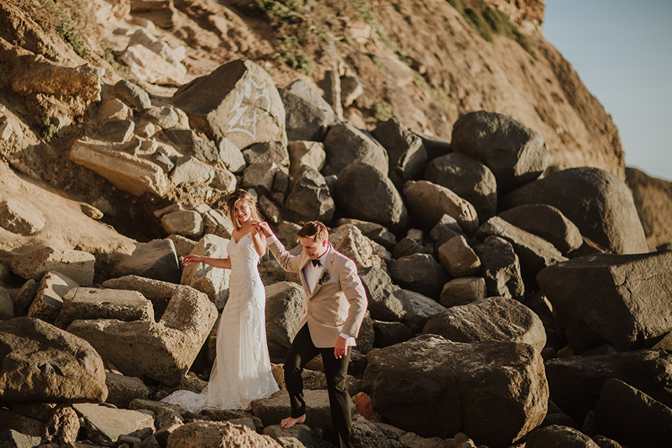 Sunset-Cliffs-Elopement-bride-and-groom-at-rocks-bride-in-a-lace-form-fitting-gown-with-thin-straps-groom-in-a-tan-suit-coat-with-black-pants-and-black-bow-tie