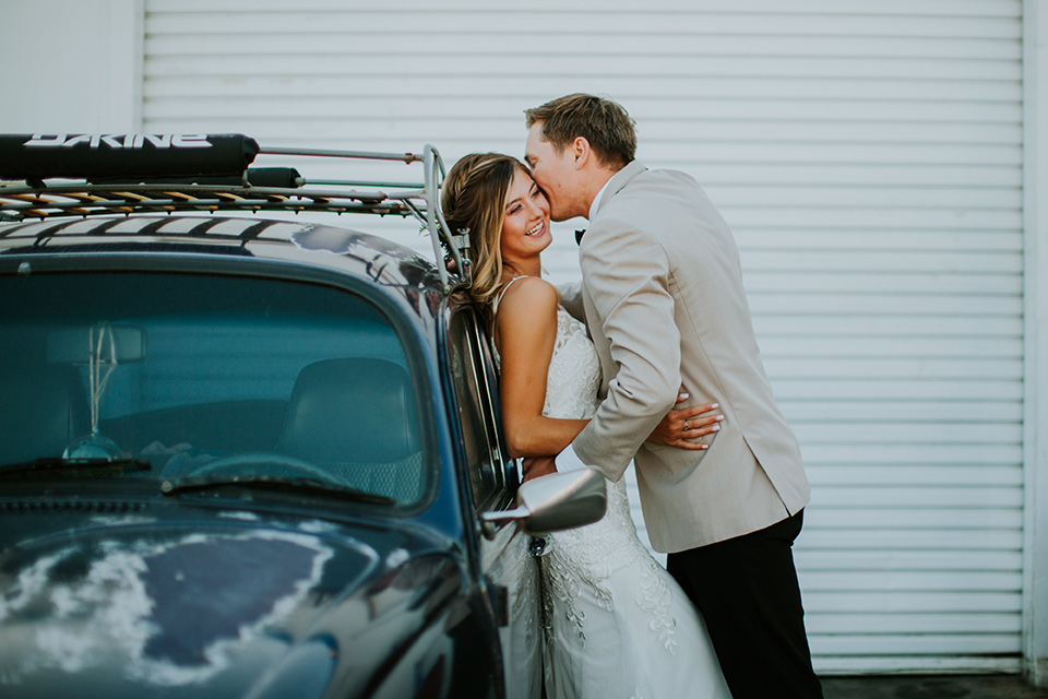 Sunset-Cliffs-Elopement-bride-and-groom-leaning-against-car-bride-in-a-lace-form-fitting-gown-with-thin-straps-groom-in-a-tan-suit-coat-with-black-pants-and-black-bow-tie