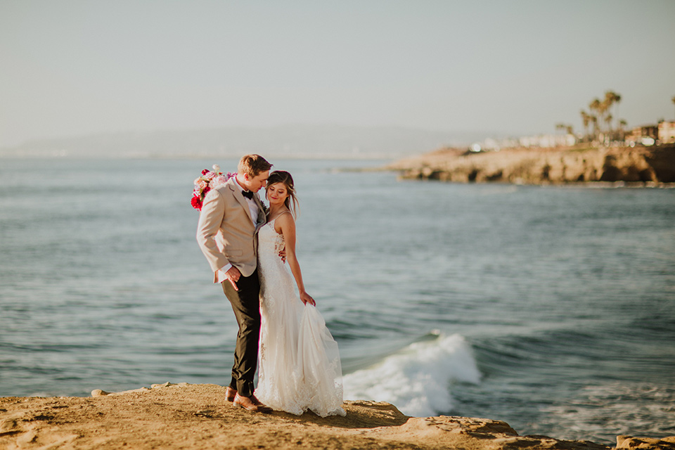 Sunset-Cliffs-Elopement-bride-and-groom-overlooking-cliffs-bride-in-a-lace-form-fitting-gown-with-thin-straps-groom-in-a-tan-suit-coat-with-black-pants-and-black-bow-tie