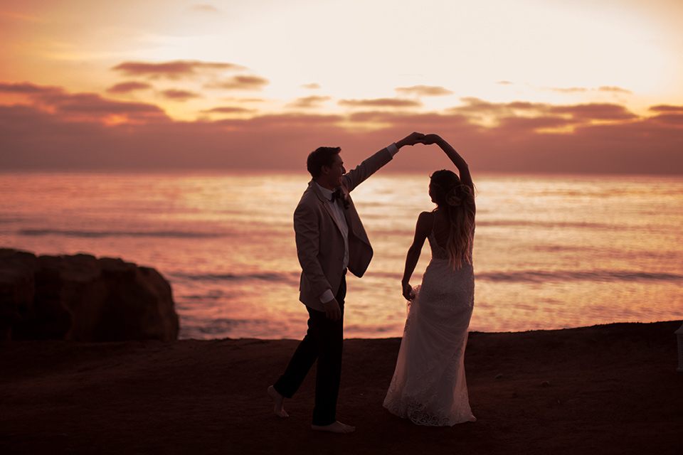 Sunset-Cliffs-Elopement-bride-and-groom-twirling-at-sunset-bride-in-a-lace-form-fitting-gown-with-thin-straps-groom-in-a-tan-suit-coat-with-black-pants-and-black-bow-tie