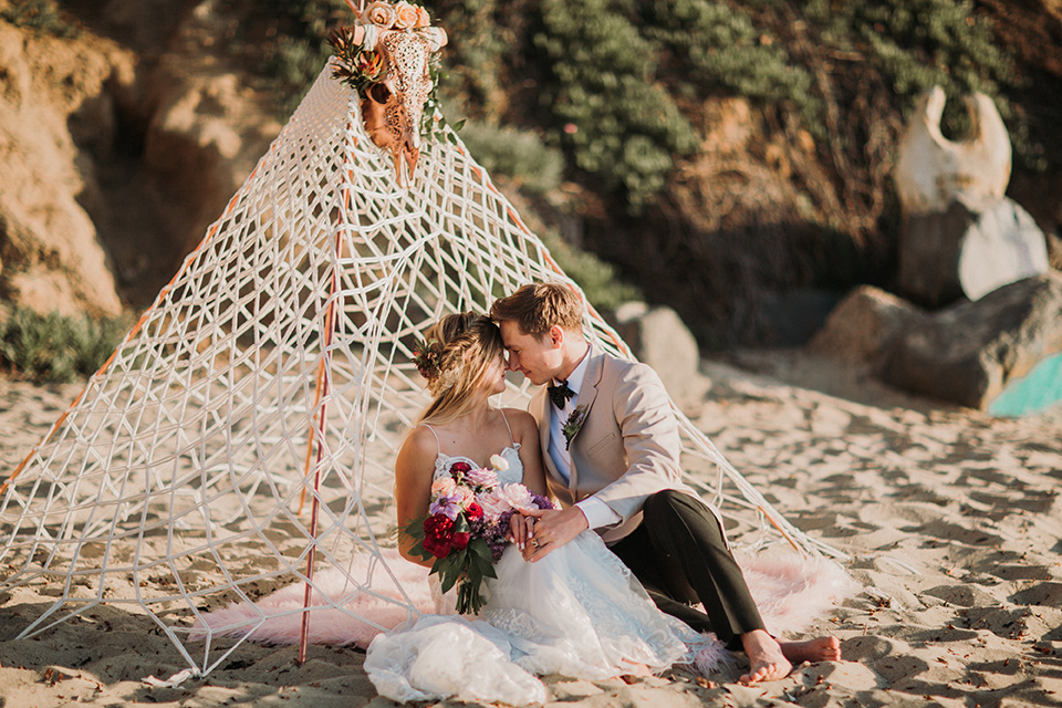 Sunset-Cliffs-Elopement-bride-and-groom-under-tent-bride-in-a-lace-form-fitting-gown-with-thin-straps-groom-in-a-tan-suit-coat-with-black-pants-and-black-bow-tie