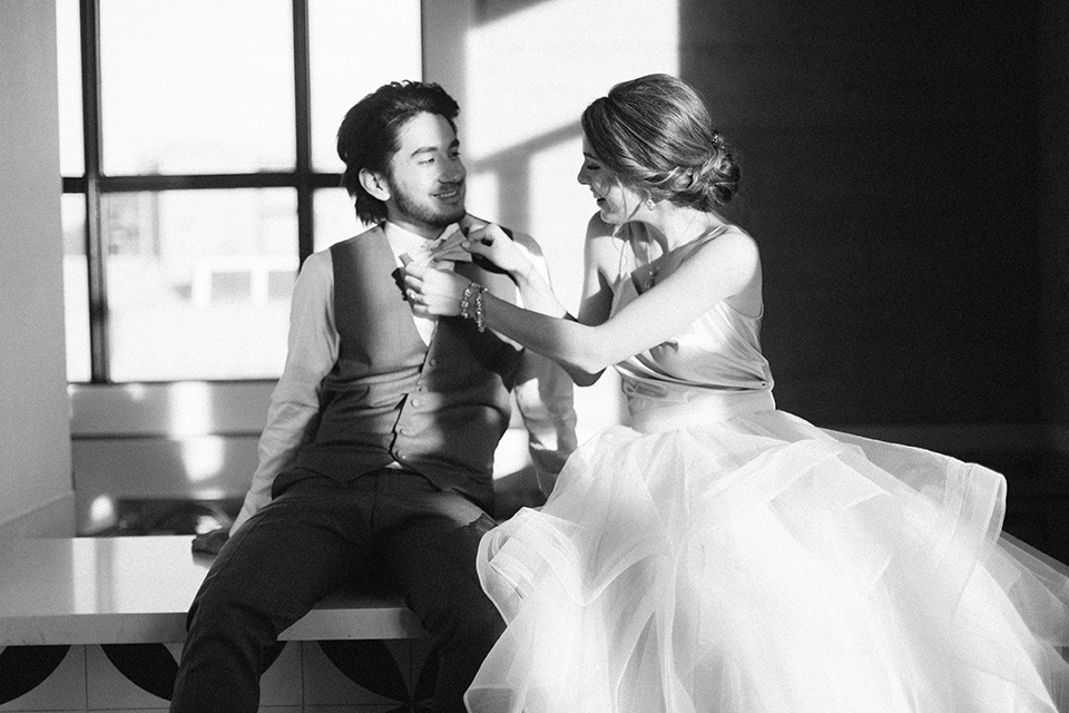 The-1912-Shoot-bride-and-groom-black-and-white-photo-laughing-groom-in-a-grey-suit-and-ivory-bow-tie-bride-in-a-tulle-ballgown-with-straps