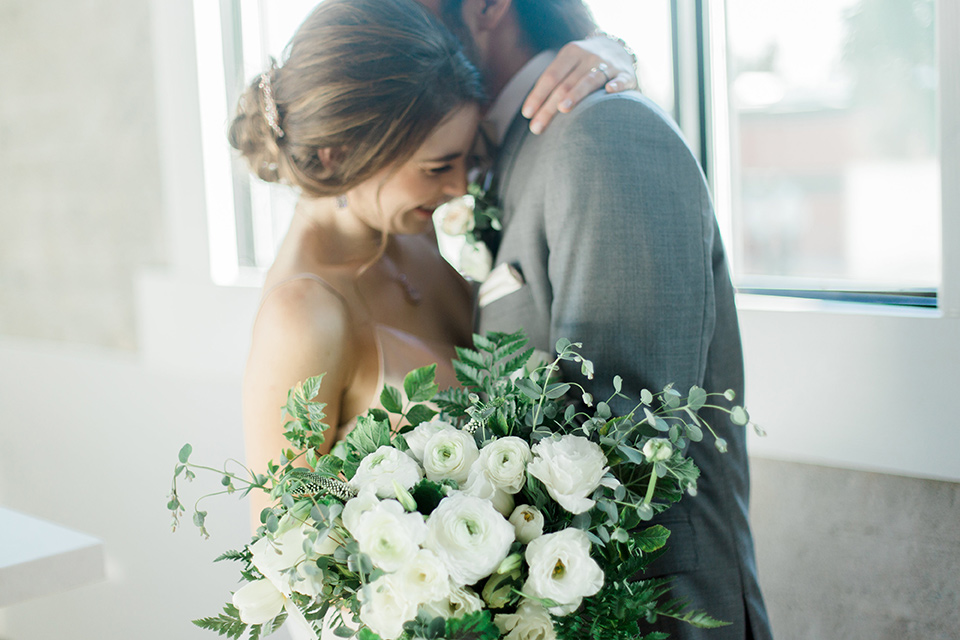 The-1912-Shoot-bride-and-groom-smiling-and-hugging-groom-in-a-grey-suit-and-ivory-bow-tie-bride-in-a-tulle-ballgown-with-straps