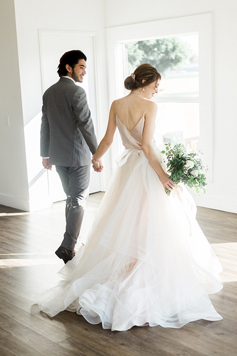 The-1912-Shoot-bride-and-groom-walking-away-bride-in-a-tulle-ballgown-with-a-low-back-and-thin-straps-groom-in-a-grey-suit-with-a-white-bow-tie